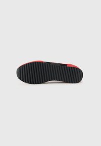 Shoe sole in black rubber with vertical grooves, accentuated by red edges. Features a textured surface for grip.