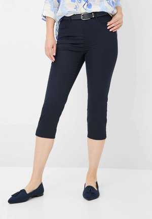 Marineblauwe cropped broek van gladde stof met een getailleerd ontwerp, voorzien van een riem met een zilveren gesp. Gepaard met marineblauwe suède instappers.