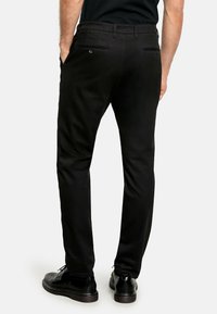 Zwarte chino's van een gladde stof, met een slim fit, achterzakken en riemlussen. Gecombineerd met zwarte schoenen en een ingestopt shirt.