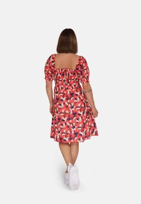 Bloemmotief jurk met korte puffmouwen, vierkante rug en smock taille. Voornamelijk rood met roze en witte accenten, knielang.