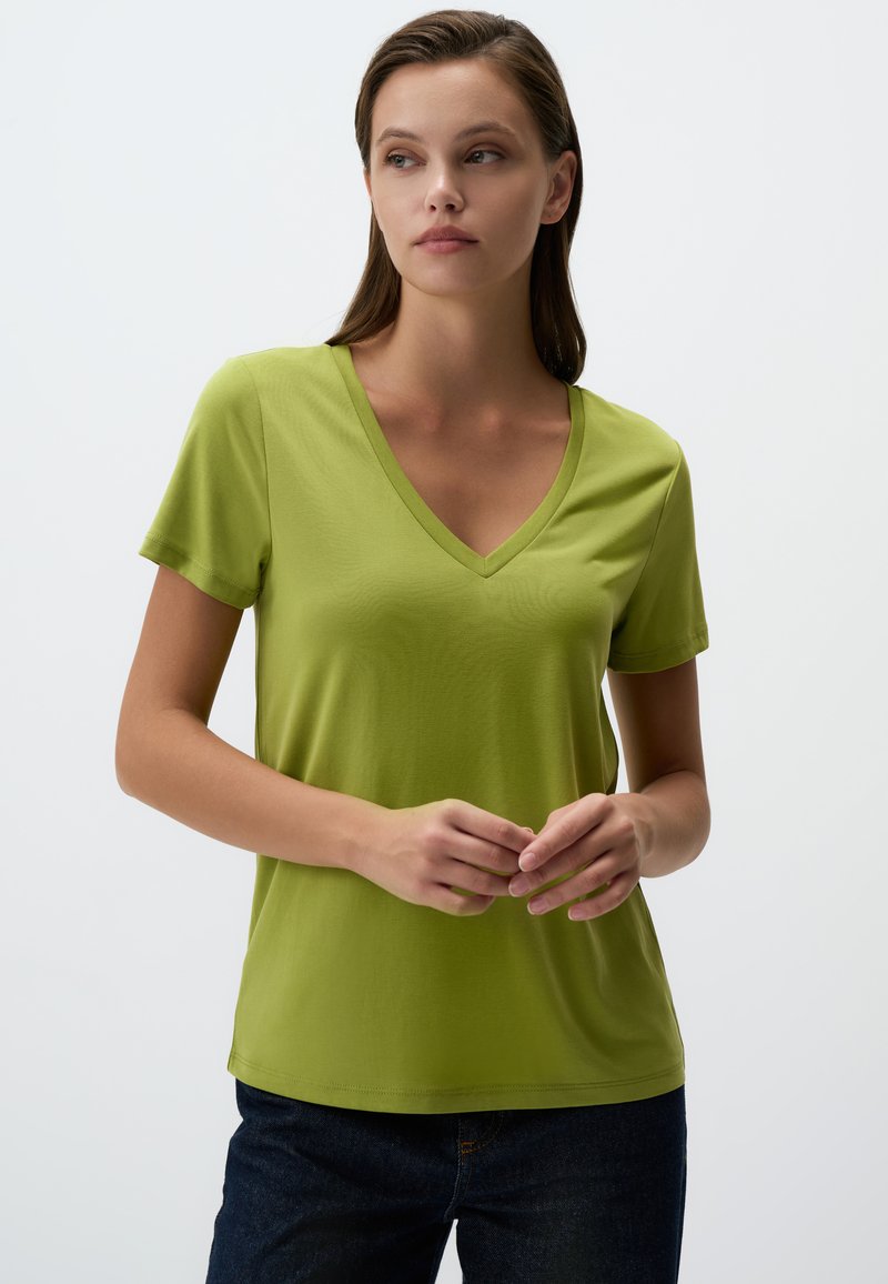 Zielona koszulka V-neck z krótkimi rękawami, wykonana z gładkiego materiału. Klasyczny krój o prostym wzorze, w połączeniu z ciemnymi spodniami.