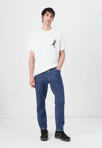 Hvid bomulds T-shirt med grafisk tryk, parret med blå denim jeans. Sorte sneakers med hvide accenter. Simpel, afslappet tøjensemble.