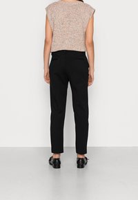 Haut en maille légère tachetée avec manches courtes, associé à un pantalon noir ajusté et des chaussures noires. Le pantalon possède des poches à l'arrière.