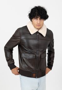 Bruine leren bomberjack met een crèmekleurige schapenvachtkraag, rits sluiting, twee voorkezen en geribbelde manchetten en onderrand.