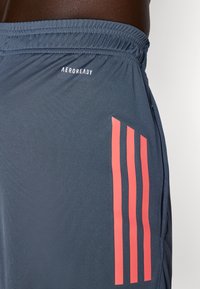 Mørkegrå sports-shorts har en tætsiddende design, en elastisk talje og tre markante koralstriber på venstre side.