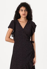 Vestido preto drapeado com mangas curtas e esvoaçantes, apresentando um padrão floral em rosa e branco. Feito de um tecido leve, inclui um laço lateral.