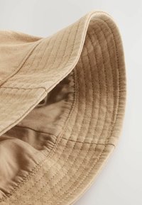 Beige Bucket Hat aus weichem Baumwollstoff mit runder Krone und breiter, weicher Krempe. Das Innere hat ein glattes Futter und dezente Stickdetails.
