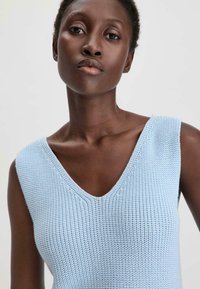 Lichtblauw mouwloos gebreid topje met een diepe V-hals, textuurstof en subtiele patronen, geschikt voor warm weer.