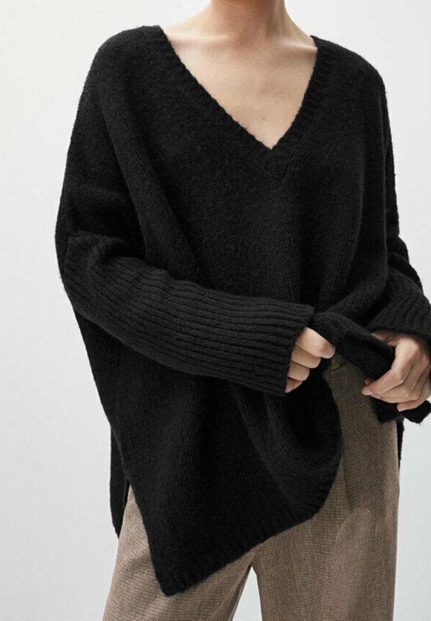 Black knitted sweater with a V-neck, loose fit, and ribbed cuffs. Soft texture, asymmetrical hemline, worn with beige checked pants.