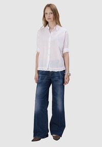 Chemise blanche boutonnée avec manches à volants, associée à un jean large bleu foncé et des chaussures à imprimé léopard. Design simple et épuré avec un contraste de textures.