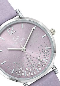 Montre ronde avec un boîtier en argent, cadran lavande avec des détails scintillants et des index métalliques, et un bracelet en cuir lavande assorti.
