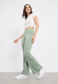 Leggings évasés vert clair en tissu doux, dotés d'une taille haute. Associés à un haut blanc ajusté à manches courtes et des baskets blanches.