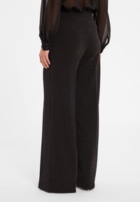Pantalons noirs à jambe large avec un motif en fil métallique, une texture lisse et des fentes sur les côtés à l'ourlet pour plus de détails.