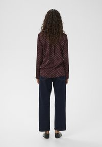 Cămașă maro cu mâneci lungi și buline albe, asortată cu blugi evazați de culoare albastru închis. Cămașa are o tiv curbat și un croi lejer.