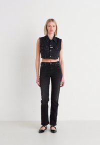 Must musta lõikega must denimvest, millel on kraega kaelus, nupud ees ja kaks rinna taskut, koos kõrge talje ja mustade teksadega. Sujuv tekstuur.