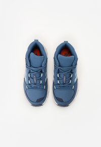 Scarpe sportive blu con tomaia in tessuto strutturato, colletto imbottito e solette rosse a contrasto. Tre strisce bianche sui lati.