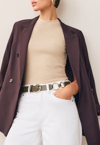 Ciemnofioletowa marynarka, beżowa prążkowana bluzka, białe dżinsy, zielony pasek ze złotymi ozdobami. Charakteryzuje się luźnym krojem i kieszeniami.