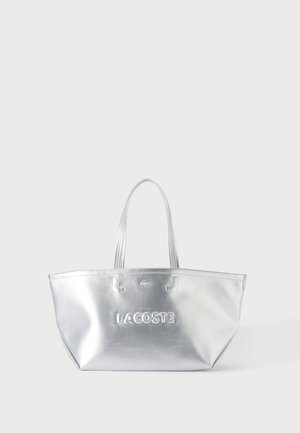 Skinnende sølv tote taske med to håndtag, med præget Lacoste-logo og lille krokodilleemblem foran i midten.