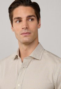 Camisa blanca con un patrón de cuadros en amarillo claro y azul. Presenta un cuello con botones y está hecha de un tejido suave.