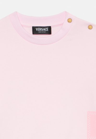Rosa bomull t-shirt med rund halsringning, med gyllene knappar som accent på axeln och en liten rosa logotyp-märke.