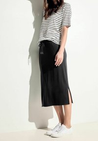 Schwarzer Maxikleid mit seitlichen Schlitzen, kombiniert mit einem schwarz-weiß gestreiften T-Shirt. Das Model trägt weiße Sneakers; der Stoff wirkt weich und bequem.
