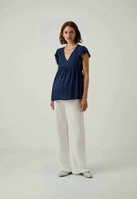 Navy blue short-sleeve top with a v-neck and gathered waist, paired with white wide-leg trousers and light-colored slip-on shoes.