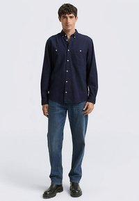 Marineblauw overhemd met knopen, kleine witte stippen, twee borstzakken en een open kraag, gecombineerd met een blauwe spijkerbroek en zwarte laarzen.