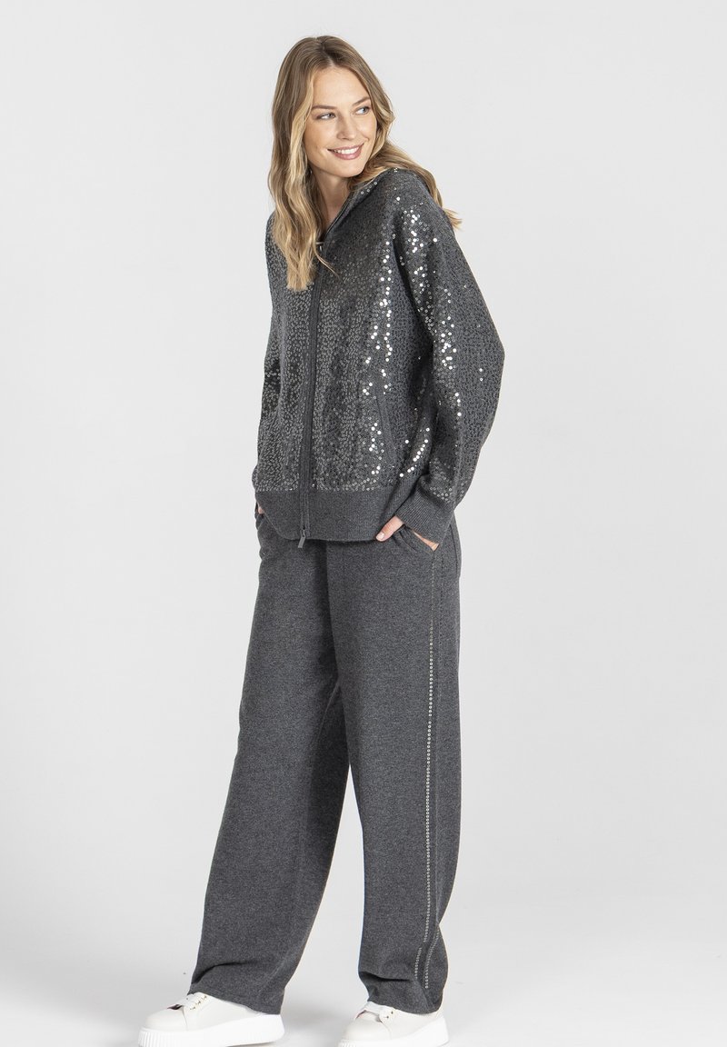 Szara bluza z kapturem zapinana na zamek, ozdobiona szarymi cekinami, połączona z luźnymi szarymi spodniami z bocznym szwem, uzupełniona białymi trampkami.