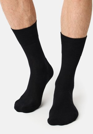 Schwarze, knöchellange Socken aus glattem Material mit gerippten Bündchen, die ein klassisches Design und eine enganliegende Passform am Fuß und Knöchel bieten.