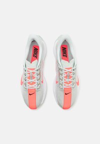 Nike hardloopschoenen met een lichtgrijs mesh bovenwerk, neon-oranje accenten, witte zool en reflecterende details in het ontwerp.