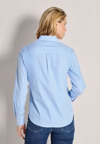 Blau-weiße gestreifte Hemdjacke mit spitzem Kragen, langen Ärmeln, Rückenteil und abgerundetem Saum. Glatte Stofftextur.