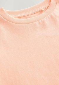 Pfirsichfarbener Baumwoll-T-Shirt mit klassischem Rundhalsausschnitt und glatter Textur, mit einem subtilen Glanz und ohne sichtbare Muster oder Akzente.