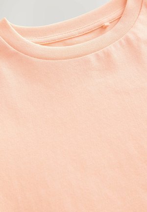 T-shirt en coton couleur pêche, doté d'un col rond classique et d'une texture lisse, avec un éclat subtil et sans motifs ni accents visibles.