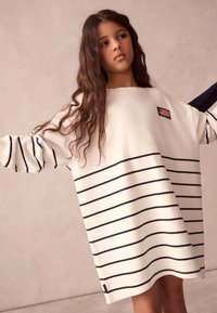 Langærmet, cremefarvet sweatshirtkjole med blå vandrette striber, der har en lille amerikansk flagpatch og blød bomuldstekstur.