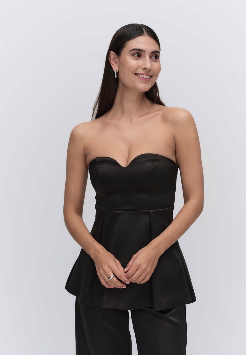 Mustat olkaimeton peplum-toppi, joka on valmistettu satiinista ja jossa on sydänkaula-aukko sekä sileä pinta, yhdistettynä mustiin housuihin.