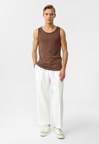 Bruine tanktop met ronde hals, gecombineerd met witte wijde broek. Model draagt lichtgekleurde sneakers. Eenvoudig, strak ontwerp.