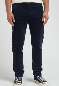 Mörkblå kordflöjlsbyxor med smal passform, med platt framdel, bältesloopar och dragkedja, ihop med svarta låga sneakers.