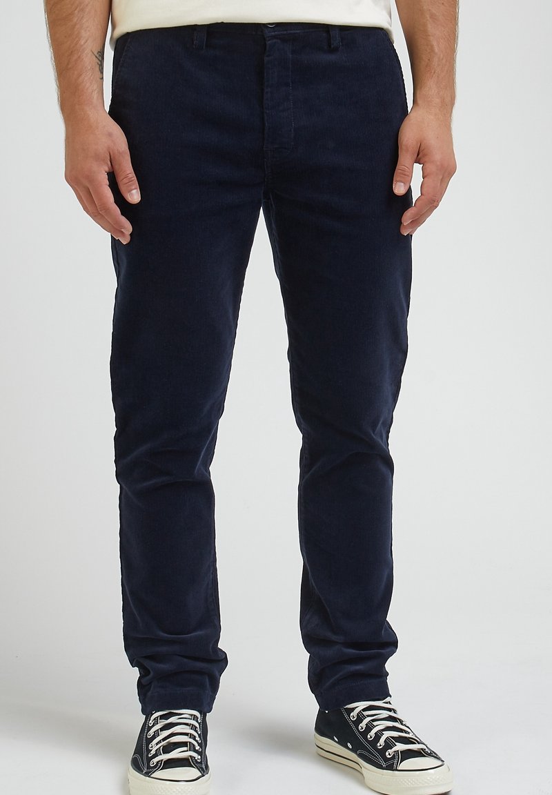 Mörkblå kordflöjlsbyxor med smal passform, med platt framdel, bältesloopar och dragkedja, ihop med svarta låga sneakers.