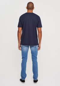 Navy cotton t-shirt with short sleeves, paired with light blue jeans. The outfit is completed with black sneakers. View from the back.