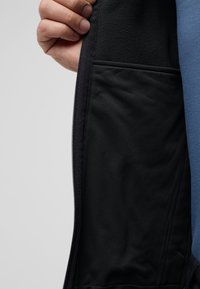 Schwarze Jacke mit Reißverschluss und einem Innenfutter mit glatter Textur und weicher Fütterung, neben einer sichtbaren, kontrastierenden blauen Außenschicht.