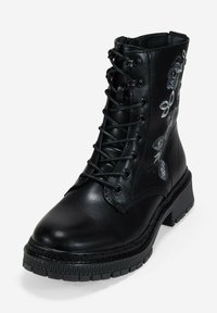 Bota de combate de cuero negro con cordones, suela gruesa y bordado floral gris en el lateral, presentada sobre un fondo blanco.