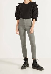 Black top with ruffles at shoulders, paired with high-waisted checkered leggings and black lace-up combat boots with thick soles.