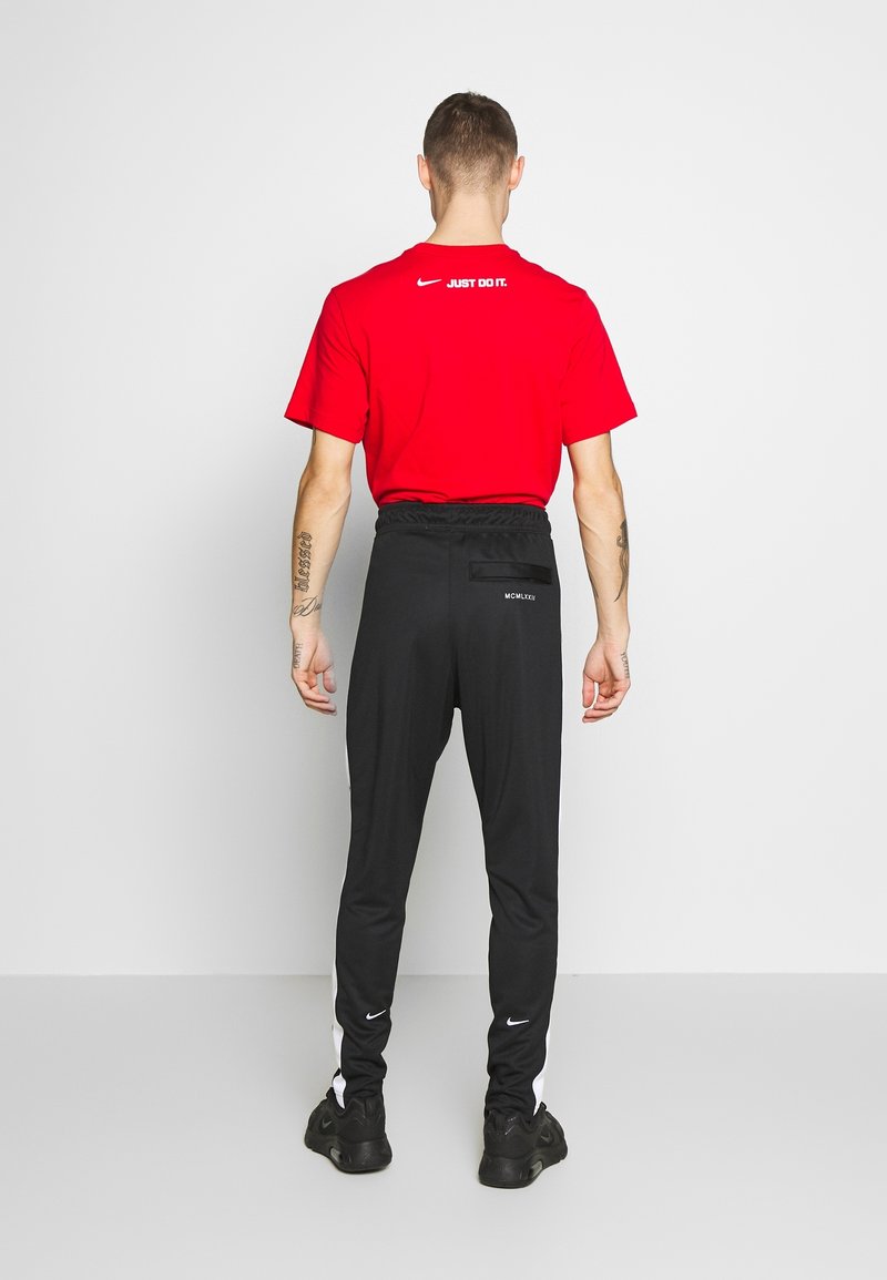 Röd Nike t-shirt med rund hals och vit "JUST DO IT" text på baksidan, kombinerad med svarta träningbyxor med vita sidostreck.