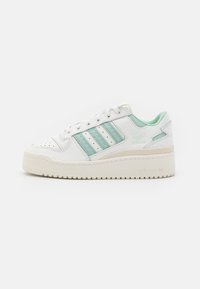 Vita sneakers med mintgröna accenter. Funktioner inkluderar tre ränder, perforerad tå och en tjock, texturerad yttersole. Varumärke är synligt.