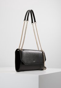 Borsa a mano in pelle nera con finitura testurizzata, tracolle a catena dorata, chiusura a patta e dettaglio con logo sulla parte anteriore.