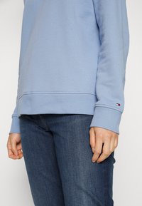 Lichtblauw sweatshirt met ribbels aan de manchetten en zoom, voorzien van een klein logopatch. Draagt bovenstaande met donkerblauwe jeans, die een gladde textuur tonen.