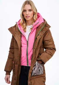 Brązowa kurtka puchowa z różowym wnętrzem, z zielonymi zamkami błyskawicznymi, kapturem i podszewką kieszeni w wzór zebry. Gładka faktura i ciepły design.