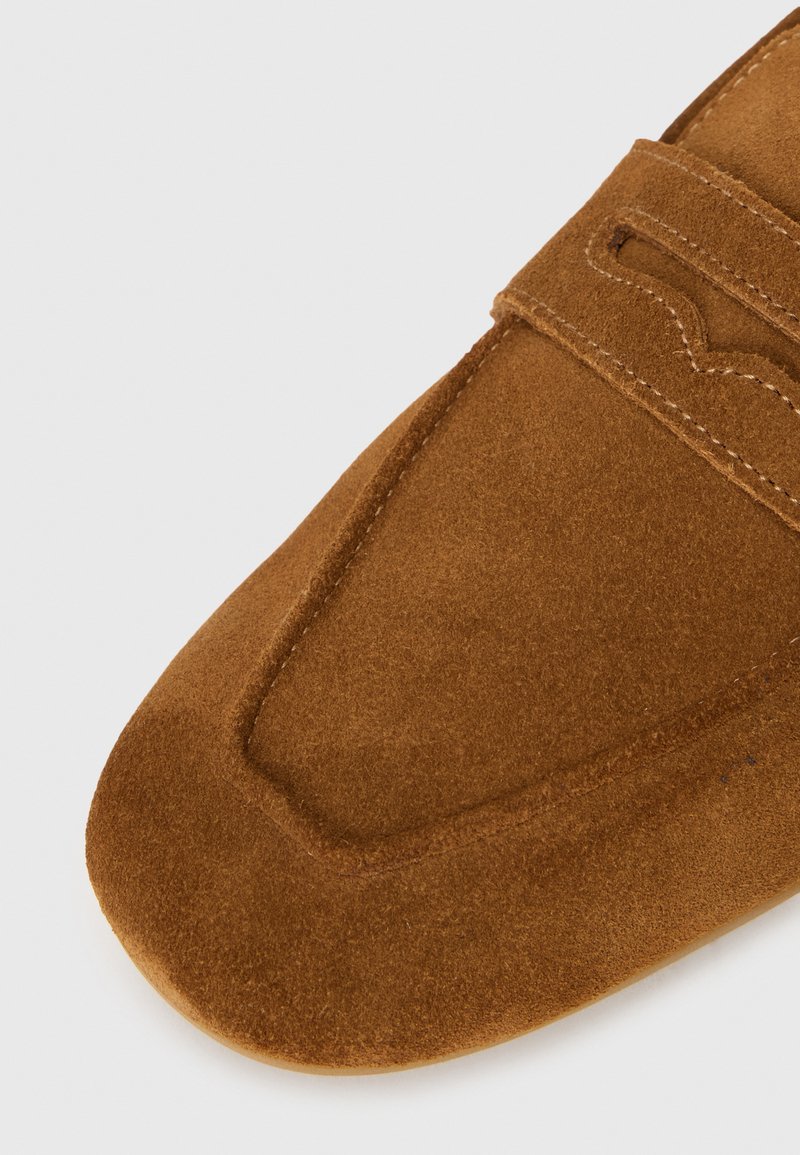Chaussure slip-on en suède marron avec un bout rond et une finition texturée, agrémentée de coutures discrètes sur la tige.