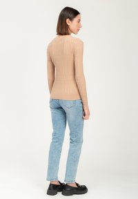 Beige gerippter Langarmshirt mit taillierter Passform, kombiniert mit hellblauen Jeans und klobigen schwarzen Schuhen, von hinten betrachtet.