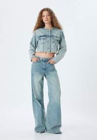 Ljust blå denimjacka med kort längd, framknappar och två bröstfickor, tillsammans med högmidjade, vida denimjeans i matchande färg.